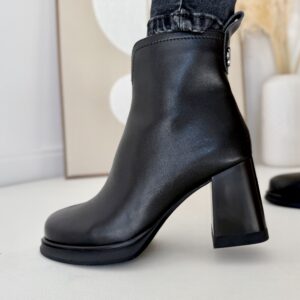 Czarne botki skórzane LULA 26 na stabilnym obcasie z ozdobą z tyłu, zapinane na zamek, wykonane z naturalnej skóry licowej, prezentowane na nodze w czarnych jeansach.