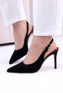 Czarne czółenka damskie na szpilce wykonane z naturalnego zamszu, z paskiem przy pięcie, noszone do białych spodni w eleganckiej stylizacji.